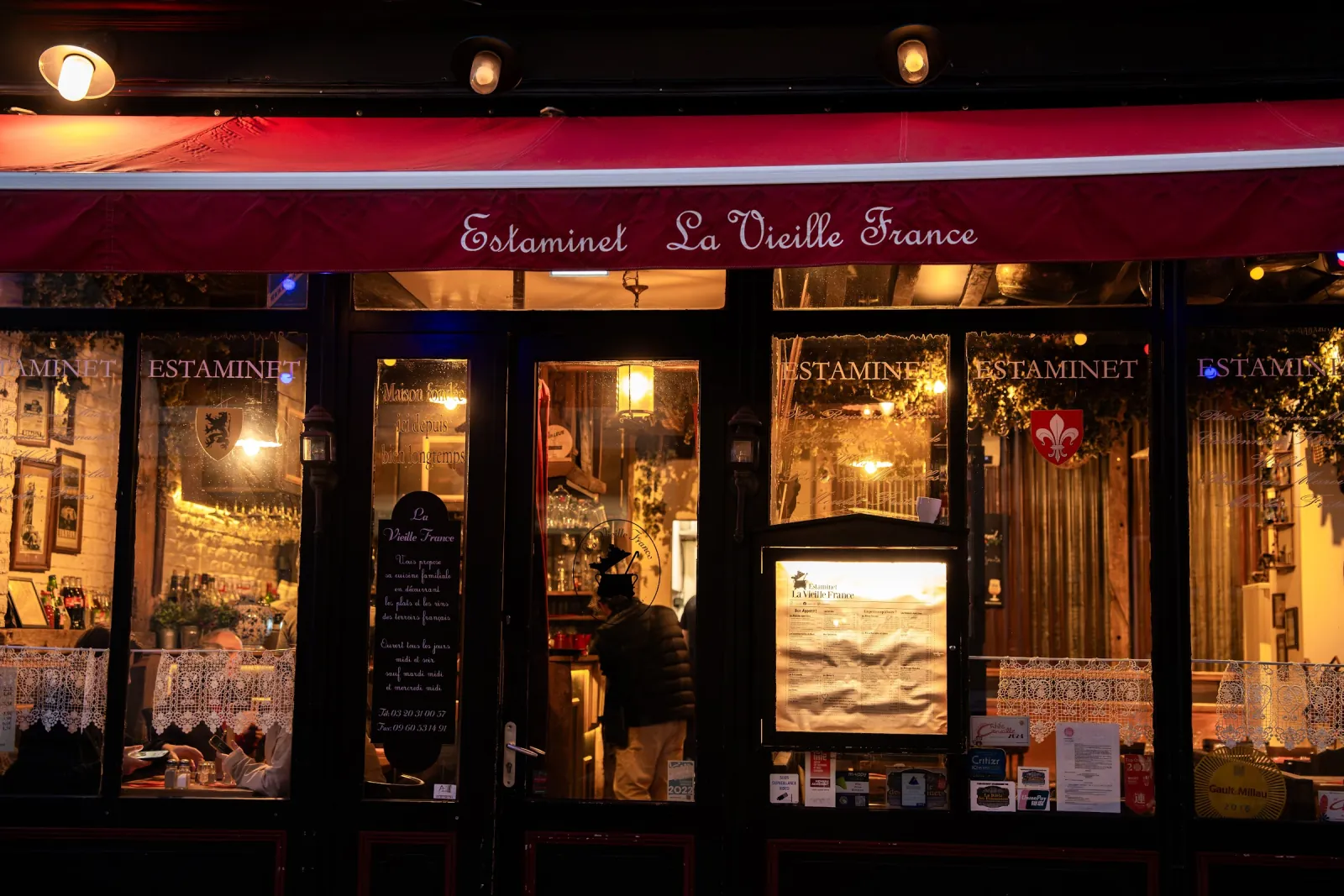 La devanture de La Vieille France, rue de Gand, store rouge et vitrines éclairées à la tombée du jour.