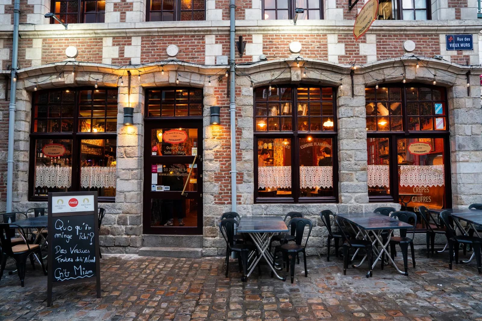 La façade de brique et de pierre blanche du Vieux de la Vieille, rue des Vieux Murs, vitrines éclairées et terrasse sur les pavés.